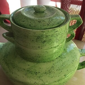 May include: A light green ceramic teapot with a matching lidded serving bowl. Both pieces have a speckled black pattern. The teapot has a curved handle and spout. The bowl has two handles.