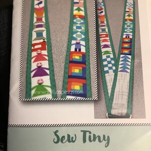 May include: A sewing pattern for a lanyard with colorful, geometric designs. The pattern includes instructions to make a 1-inch x 36-inch lanyard. The image features the text "Sew Tiny" and the website address "www.quiltscapesqs.com".