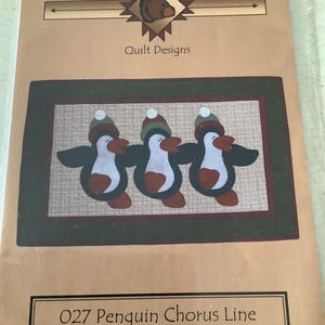 May include: A quilt design package from "The Wooden Bear" featuring a penguin chorus line. The finished quilt size is approximately 30" x 19". The design includes three penguins wearing hats, with a brown and green border.