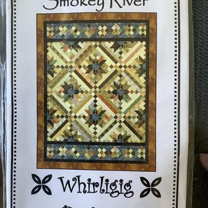May include: A quilt pattern titled "Smokey River" by Whirligig Designs. The quilt design features a geometric pattern with star-like shapes in shades of brown, green, and yellow. The pattern is framed by a brown border and a dotted white border.