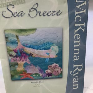 May include: A quilt pattern titled "Sea Breeze" by McKenna Ryan. The pattern features a blue fish swimming through a coral reef. The pattern is for a quilt measuring 12" x 17" and is part of the "Building Blocks" series.