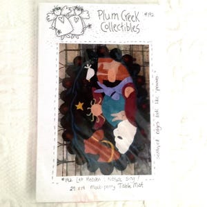 May include: A pattern for a 27 by 19 inch mock-penny table mat featuring a colorful design with a bird, sun, and stars. The pattern is titled "Let Heaven Nature Sing!" and is from Plum Creek Collectibles #192. The edges of the mat are scalloped and look like pennies.