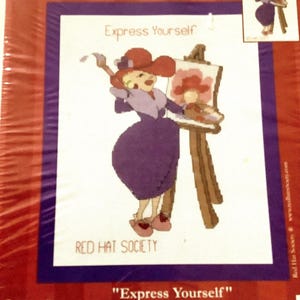 May include: A Red Hat Society counted cross stitch kit. The design features a cartoon woman in a purple dress and red hat painting on a canvas. The finished size is 8" x 10". The text "Express Yourself" is displayed.