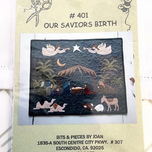 May include: A craft kit titled "Bits & Pieces by Joan" featuring a nativity scene. The image shows a detailed quilt with angels, a star, and figures around a manger. The kit includes the text "Our Savior's Birth".
