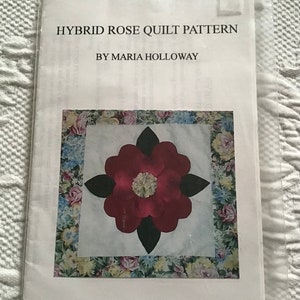 May include: A white paper pattern with a floral border and a red rose in the center. The text "HYBRID ROSE QUILT PATTERN BY MARIA HOLLOWAY" is printed at the top.