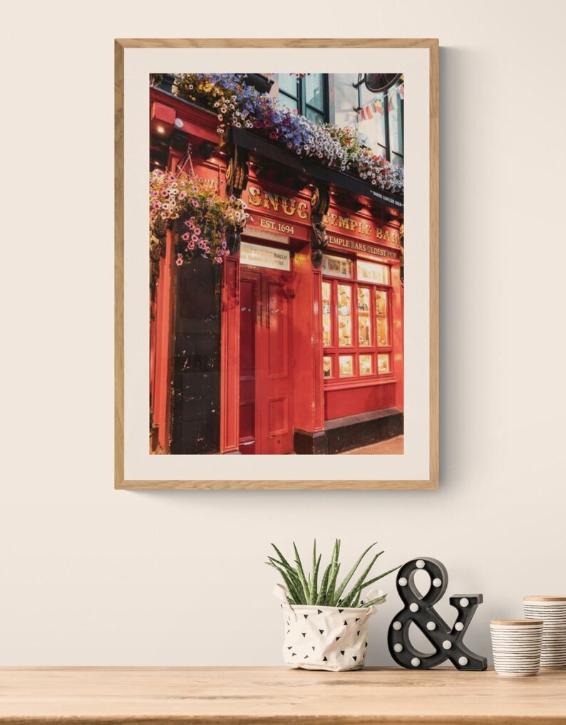 May include: A red brick building with a sign that reads "The Snug Temple Bar" and "Est. 1694". The building is decorated with hanging flower baskets and has a red door.