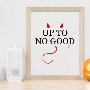 Puede incluir: Una impresión enmarcada con el texto "UP TO NO GOOD" en letras negras con una cola y cuernos de diablo rojos. Una calabaza tallada se encuentra sobre una superficie de madera junto a la impresión enmarcada.