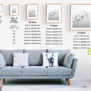 May include: A white wall with a framed black and white photo of a handwritten signature with the text "Jacob Routier" above the signature. The photo is hanging on the wall above a gray couch with white pillows. The wall also has a chart of different print sizes and ratios for framing photos.