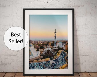 May include: A framed photograph of a cityscape with a mosaic-tiled building in the foreground. The building has a tall, pointed tower with a cross on top. The city skyline is visible in the background, with a hazy sky.