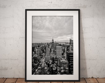 Könnte beinhalten: Schwarzweißfoto einer Stadtlandschaft mit hohen Gebäuden und einem bewölkten Himmel. Das Foto ist in einem schwarzen Rahmen gerahmt.