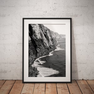 May include: Black and white photograph of a rocky coastline with crashing waves. The photo is framed in a black frame.