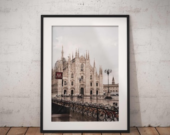 May include: A framed photograph of the Duomo di Milano, a large cathedral in Milan, Italy. The cathedral is made of white stone and has many spires. The photo was taken on a cloudy day and shows a group of bicycles parked in the foreground.