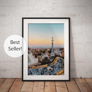 May include: A framed photograph of a cityscape with a mosaic-tiled building in the foreground. The building has a tall, pointed tower with a cross on top. The city skyline is visible in the background, with a hazy sky.