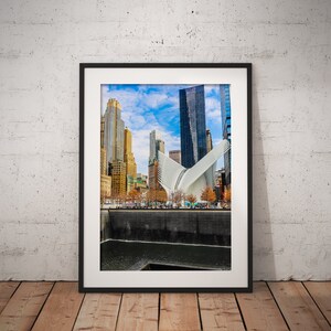 May include: A framed photograph of the 9/11 Memorial & Museum in New York City. The photo shows the reflecting pools and the surrounding skyscrapers.