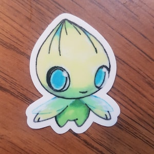 Może przedstawiać: Naklejka z postacią z kreskówki o żółtej głowie, zielonym ciele i niebieskich oczach. Postać ma skrzydła i mały uśmiech.