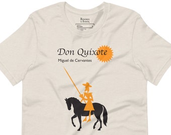 May include: A beige t-shirt featuring a black silhouette of Don Quixote riding a horse. The text "Don Quixote" and "Miguel de Cervantes" is printed in black on the shirt. A yellow sun graphic is printed next to the text.