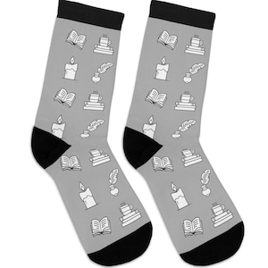 May include: A pair of gray socks with black heels and toes. The socks are patterned with white illustrations of books, candles, coffee cups, and quills. These socks are a great gift for book lovers.