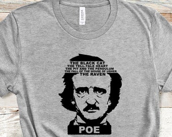Può includere: Una maglietta grigia con una grafica in bianco e nero di Edgar Allan Poe e la parola "POE" sotto. Sopra il ritratto ci sono i titoli delle sue opere: "Il gatto nero", "Il cuore rivelatore" e "Il corvo".