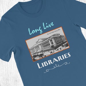 K&ouml;nnte beinhalten: Ein blaues T-Shirt mit einem Vintage-Bild der New York Public Library und dem Text "Long Live Libraries" in einer kursivschrift.
