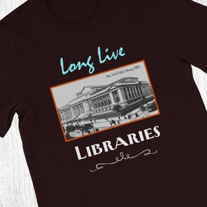 K&ouml;nnte beinhalten: Ein dunkelmarrones T-Shirt mit einem Vintage-Schwarzwei&szlig;bild des Geb&auml;udes der New Yorker &ouml;ffentlichen Bibliothek. Der Text "Long Live Libraries" ist in Wei&szlig; unter dem Bild mit einem dekorativen Schn&ouml;rkel gedruckt.