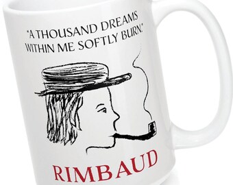 Puede incluir: Taza de cerámica blanca con una ilustración en blanco y negro de una persona con un sombrero y fumando una pipa. El texto "A thousand dreams within me softly burn." y "Rimbaud" están impresos en la taza.