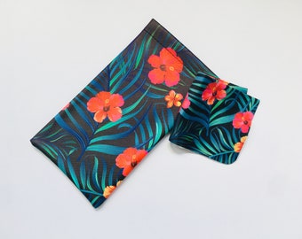 May include: A black and blue tropical print glasses case with a matching smaller pouch. The case features red and orange hibiscus flowers and green palm leaves.