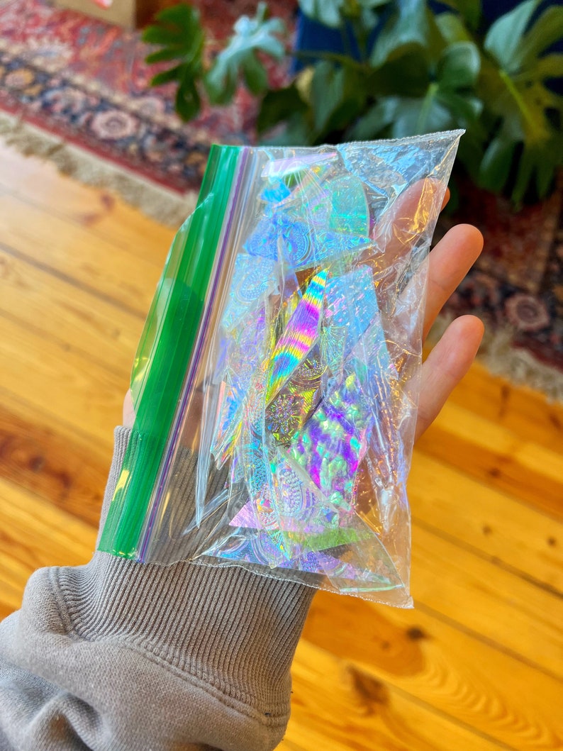 May include: A clear plastic bag filled with iridescent holographic stickers. The stickers are in various shapes and sizes, with a rainbow of colors.