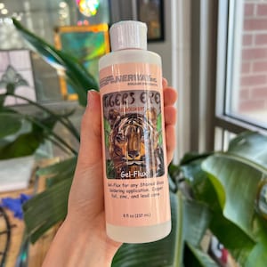 Op de afbeelding: Een fles "Tiger's Eye" Gel-Flux voor het solderen van glas-in-lood. Het etiket toont een tijgerillustratie en productinformatie. De fles bevat 237 ml flux.