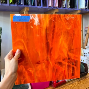 Puede incluir: Una lámina de vidrio coloreado naranja con un patrón de espiral. La lámina mide 30,5 x 30,5 cm y tiene la fecha 05-04-96 escrita en ella.