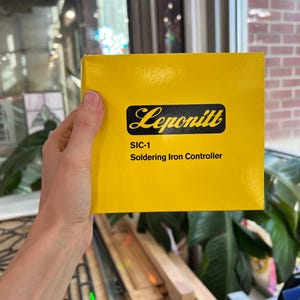 May include: A bright yellow box with the brand name "Leponitt" in black script. The box also features the text "SIC-1 Soldering Iron Controller" in black. The box is held by a person.
