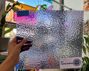 May include: A clear, textured glass sheet with an iridescent sheen. The sheet is held in a hand and has a label that reads "English Muffin 218".