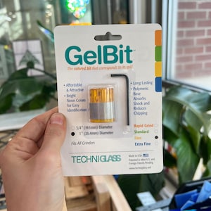 May include: A package for a GelBit glass grinding bit. The package is white with a teal logo and text. The bit is yellow and silver. The package includes the text "Affordable & Attractive" and "Bright Neon Colors for Easy Identification". The bit is 1 inch (25.4mm) in diameter.