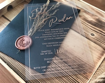 May include: A clear acrylic wedding invitation with a black background and gold lettering. The invitation reads "Seda and Ruslan" and includes the date "16.06.2023" and the time "14 Uhr".