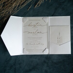 May include: A white wedding invitation with a laser-cut design featuring the names "kristin" and "marlon" in gold script. The invitation details the wedding date as "Saturday, the twenty fifth day of September 2021" and the location as "The Waterview at Port Jefferson Country Club".