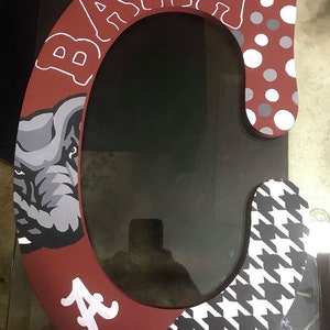 May include: A large wooden letter C painted in a red, white, and black color scheme. The letter is decorated with a houndstooth pattern, polka dots, and an elephant graphic. The word "BAMA" is written in white on the top of the letter.