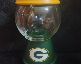 May include: Green and yellow painted glass gumball jar with a green and white "G" logo.
