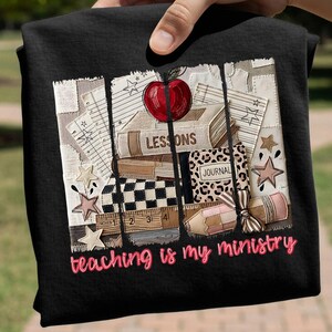 Könnte beinhalten: Ein schwarzes T-Shirt mit einem Grafikdruck aus gestapelten Büchern mit der Aufschrift Lessons und Journal, einem roten Apfel, einem Lineal und einem Bleistift. Das Design enthält Sterne und den Text teaching is my ministry in rosa Schreibschrift.