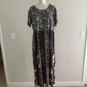 Peut inclure: Une robe longue à manches courtes présentant un motif patchwork composé de motifs cachemire noirs et blancs, de pois noirs et blancs et d'imprimés floraux roses. Le vêtement possède une encolure ronde et une jupe longue froncée.