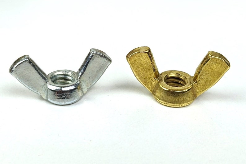 May include: Two wing nuts, one silver and one gold, are displayed against a white background. The wing nuts have a threaded center and two flat, wing-shaped extensions for easy tightening by hand. These fasteners are commonly used in various applications.