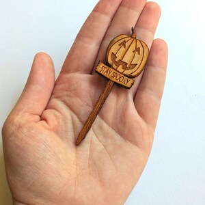 May include: A wooden Halloween decoration with a carved pumpkin face and the text "STAY SPOOKY" on a sign.