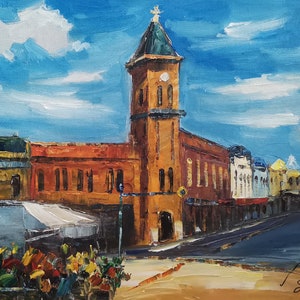 May include: An oil painting depicts a cityscape with a prominent orange-brown building featuring a tall tower with a green roof and a cross. The sky is blue with white clouds. Other buildings in the scene are yellow, white, and blue. A street and sidewalk are in the foreground.