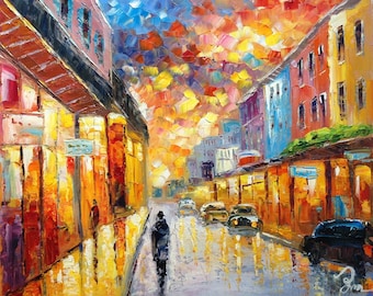 May include: A colorful oil painting of a city street at night. The buildings are brightly lit and the sky is filled with colorful clouds. A single person walks down the street.