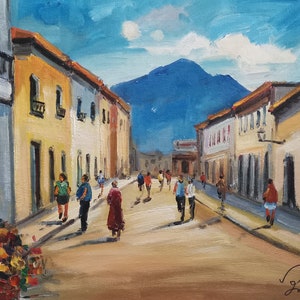 May include: Oil painting of a sunlit street scene with buildings and people. The buildings are painted in shades of yellow, orange, and white, with red-tiled roofs. A mountain is visible in the background under a blue sky. People are walking on the street.