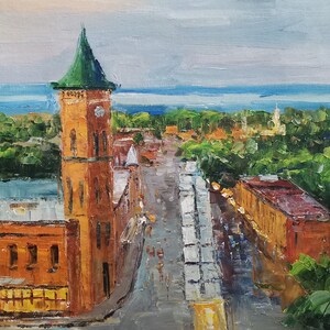 May include: An oil painting depicts a cityscape with a tall, orange brick clock tower topped with a green roof. A road leads through the town, lined with buildings and trees. The sky is overcast, and the painting has a textured, impressionistic style.