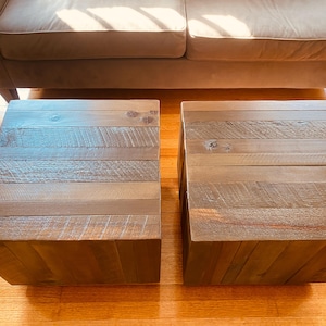 May include: Two square side tables constructed from horizontal planks of dark brown reclaimed wood. Each table features a flat top surface with visible wood grain, knots, and a textured finish, forming a solid cube shape with vertical side panels.