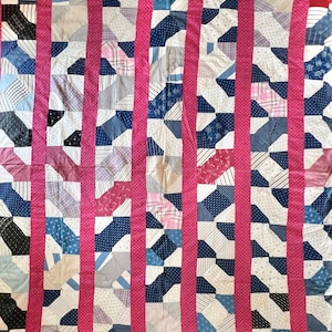 May include: A handmade quilt with a patchwork design. The quilt features a variety of fabrics in blue, white, pink, and gray, arranged in a geometric pattern. Vertical pink stripes with white polka dots separate the patchwork sections. The quilt is bordered with a solid pink fabric.