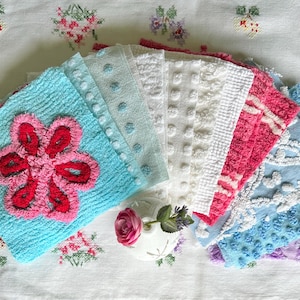 May include: A collection of square fabric swatches featuring various textures and patterns, including a bright blue piece with a large pink flower, light blue and white dotted designs, and pink and blue pieces with intricate raised floral embroidery.