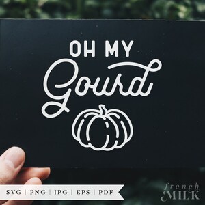 May include: A black sign with white text that reads "Oh My Gourd" with a white outline of a pumpkin below the text.