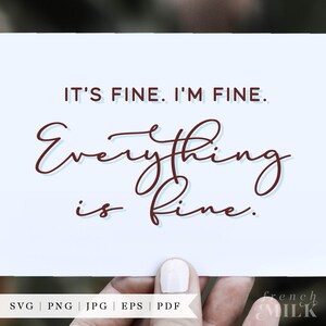 May include: A white card with the text "IT'S FINE. I'M FINE. Everything is fine." written in brown cursive script. The card is being held by a hand with white nail polish.
