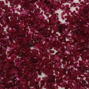 May include: A pile of small, red ruby gemstones. The rubies are irregularly shaped and have a shiny, polished finish.